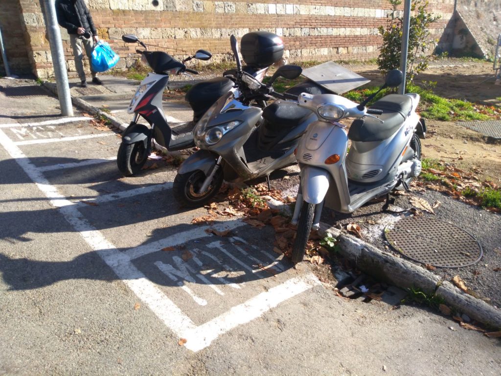 Parcheggio motorini "a cavallo" del marciapiede: per non farli cadere si rischia la multa
